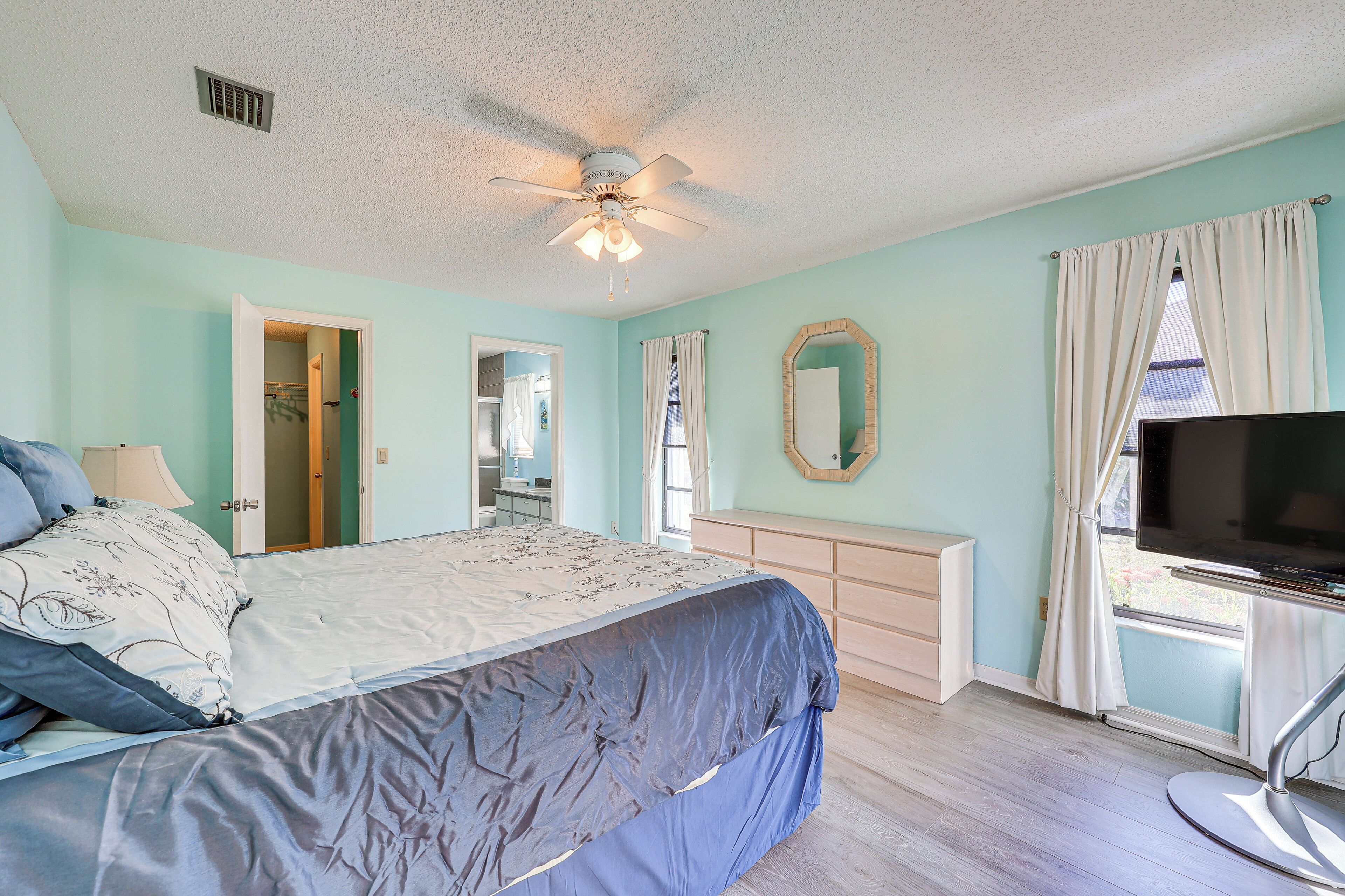 A bedroom with a bed, a ceiling fan, a dresser, a TV, and a window with curtains.
