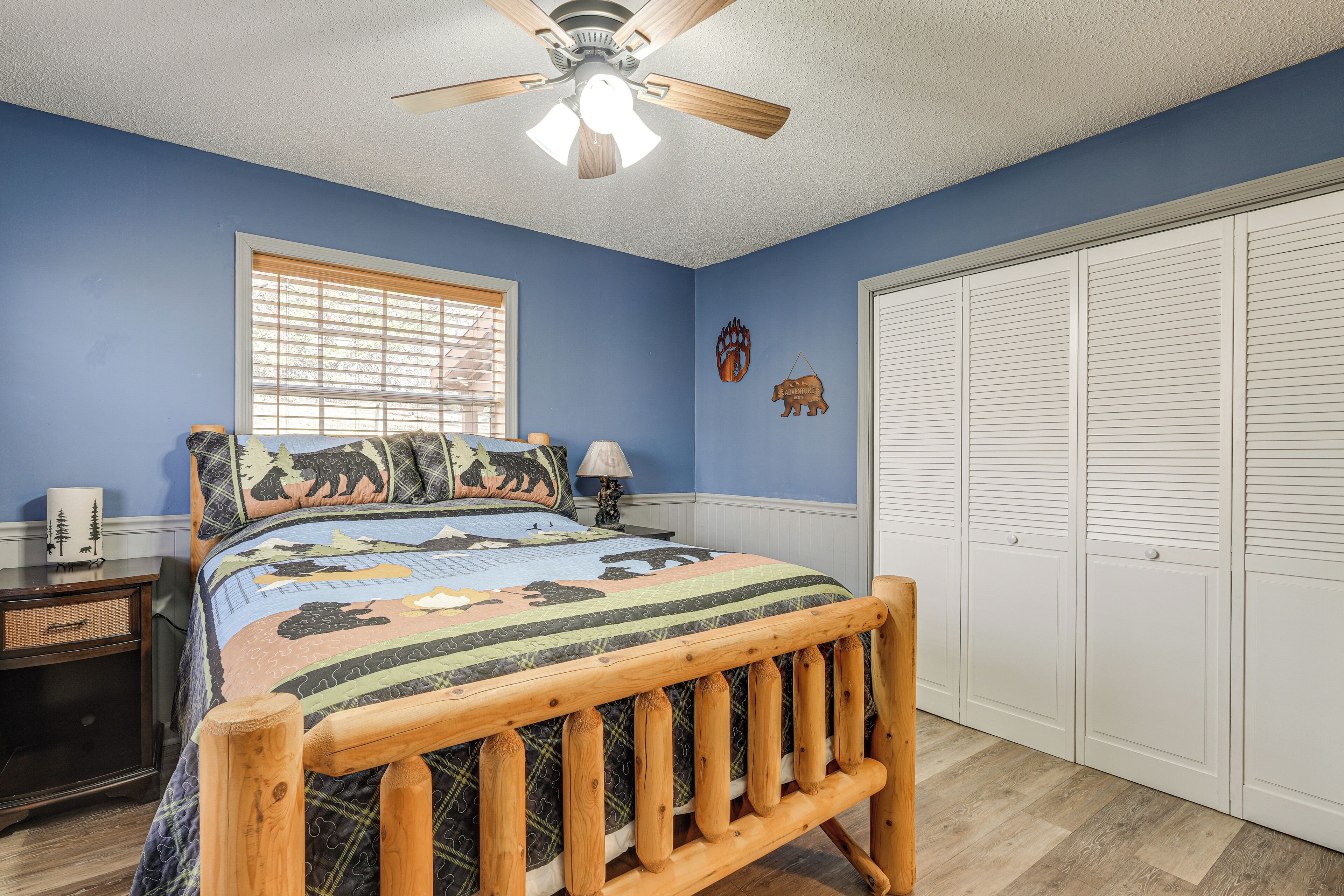 Un dormitorio con cama de madera, ventilador de techo, ventana con persianas, armario y decoración en la pared.