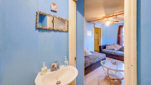 A bathroom with a sink, mirror, and toiletries. A bedroom with a bed and a small round table is visible through an open door. - Countryside Escape, 8 Mi to Fvsu & Main Street! (Fort Valley)