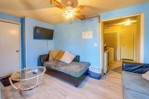 A compact living space with a sofa, a glass table, a ceiling fan, and a television mounted on the wall.