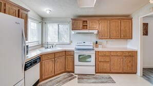 Una cocina con armarios de madera, un refrigerador blanco, un lavavajillas, una estufa y una ventana con persianas.