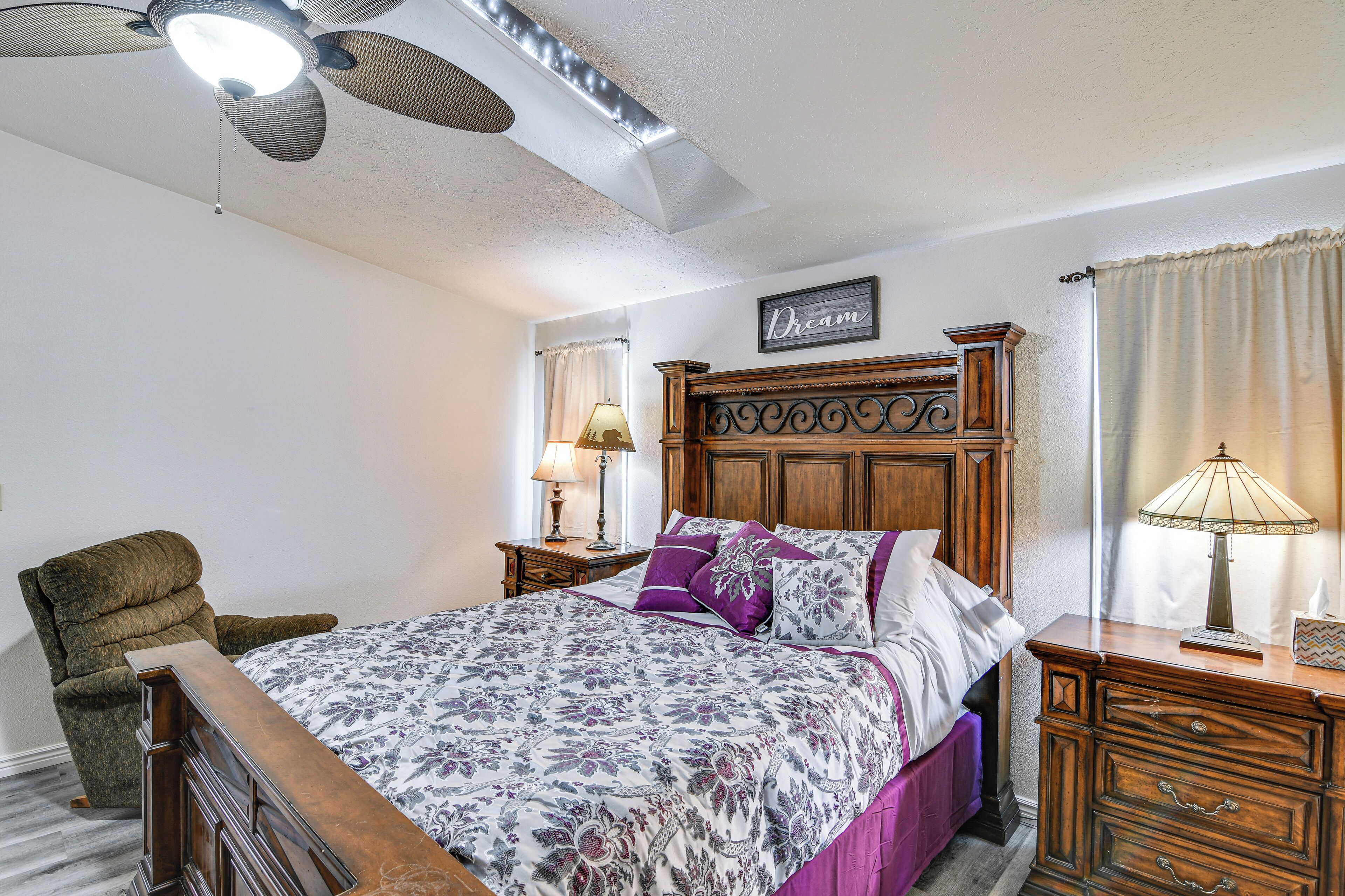 Un dormitorio con cama, una silla, mesita de noche, cómoda y ventilador de techo, además de una lámpara de pared.