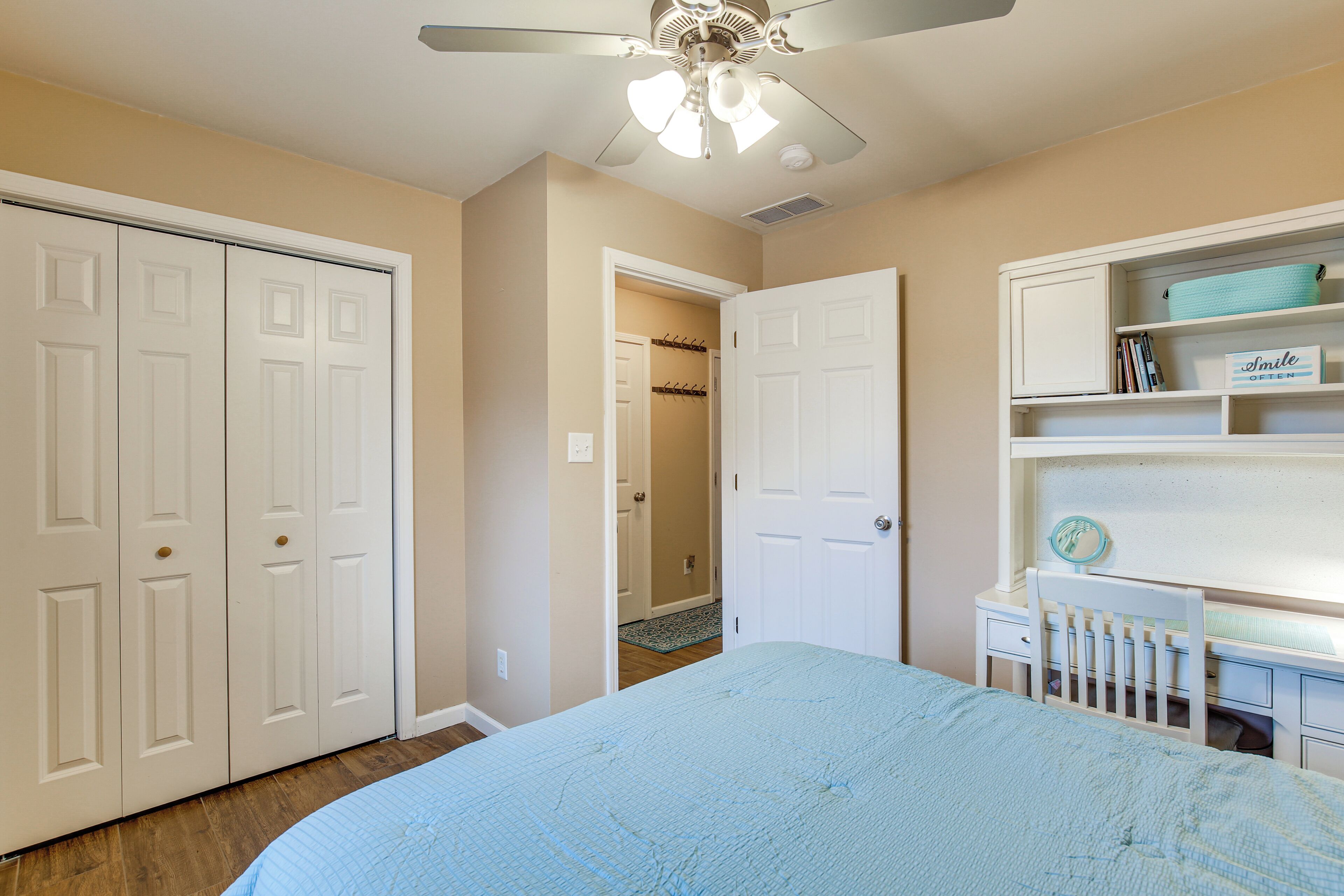 A bedroom with a bed, a desk, a chair, a wardrobe, and a ceiling fan.