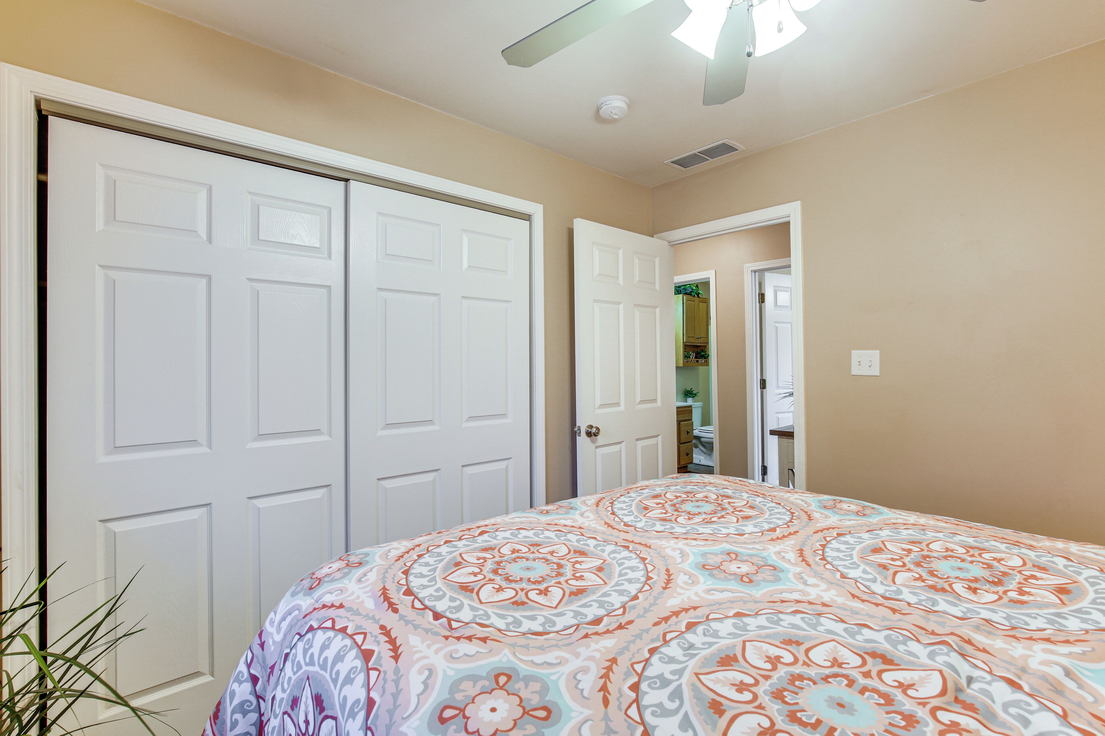 A bedroom with a large bed, two white doors, and a ceiling fan.