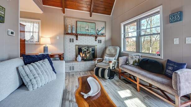 A cozy living room with a fireplace, a sofa, a bench, and a large window.