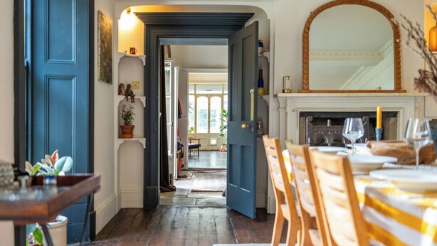 A dining area with a wooden table and chairs, a fireplace, and a hallway leading to another room. - Stunning 8-Bedroom Home in Painswick (Painswick)