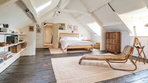 A bedroom with a wooden bed, a wicker chair, a wooden wardrobe, and a skylight. - Stunning 8-Bedroom Home in Painswick (Painswick)
