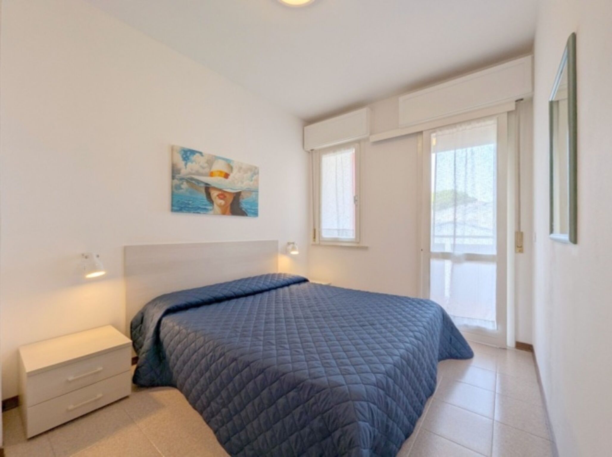 A bedroom with a bed, a nightstand, a painting, and a window.