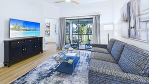 A living room with a large TV, a ceiling fan, a sofa, and a view of the outdoors. - Golf, Dining, and Convenience Awaits     🚀 (Titusville)