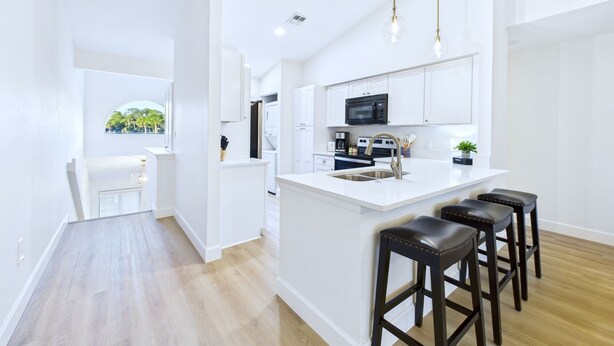 A modern kitchen with white cabinetry, a central island with stools, and a view of greenery outside. - Golf, Dining, and Convenience Awaits  🚀 (Titusville)