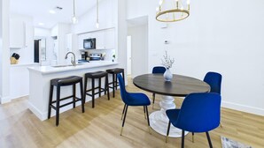A modern kitchen with white cabinets, a central island with stools, and a dining area with a round table and blue chairs. - Golf, Dining, and Convenience Awaits  🚀 (Titusville)