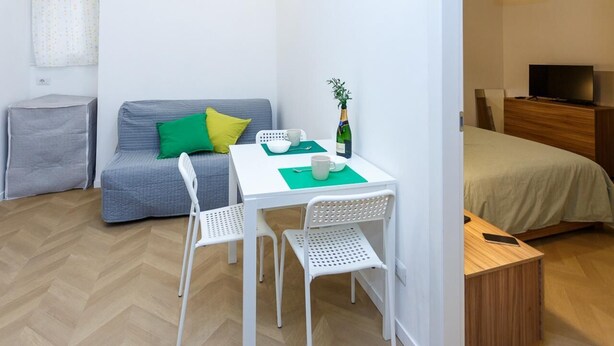 Ein gemütliches Hotelzimmer mit grauem Sofa, einem kleinen Esstisch mit zwei Stühlen, einem Bett, einem Fernseher und einem Holzbeistelltisch.