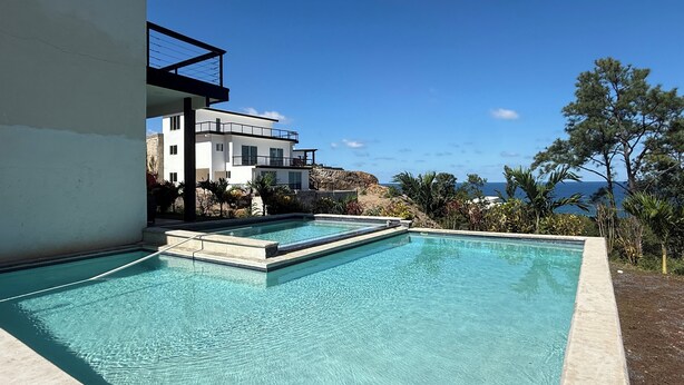 Zona de piscina moderna amb aigua blava cristal·lina, un edifici blanc amb balcons i vista a l'oceà.