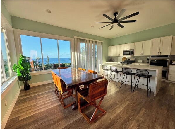 A spacious kitchen with white cabinets, a central island with bar stools, and a view of the ocean through large windows. - Ocean Crest Luxury Villa - 6BR w/Pool (Camp Bay)