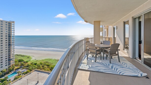 Un balcon avec vue sur la plage, une table avec des chaises et une piscine en arrière-plan.