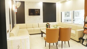 A living room with a beige sofa, two chairs, a coffee table, and a TV mounted on the wall. - Hotel Devki Inn (Gorakhpur)
