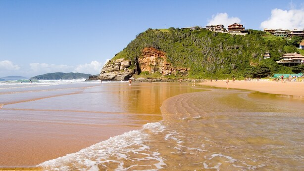A beach with clear water, a sandy shore, and buildings on a hill in the background. - Flats dos Fernandes  (Búzios)