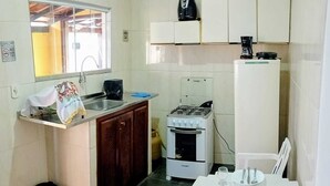 A compact kitchen with a gas stove, a sink, and a small dining table set for two. - Flats dos Fernandes  (Búzios)