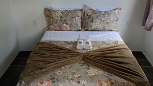 A neatly made bed with floral bedding, a brown blanket, and a pair of white slippers. - Flats dos Fernandes  (Búzios)