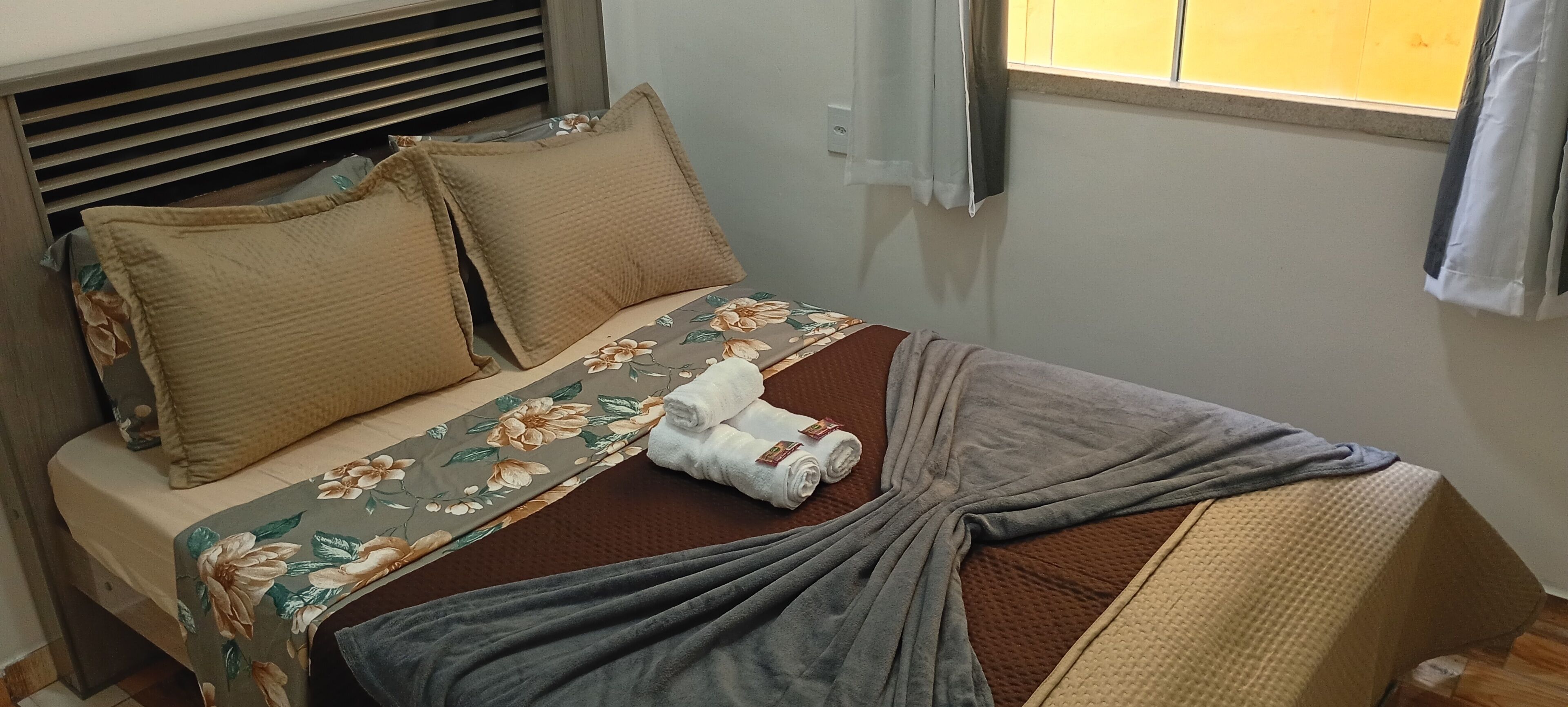 A neatly made bed with floral bedding, a grey blanket, and two beige pillows.