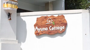 Ein Holzschild mit einem Häuschen-Symbol und dem Schriftzug 'Ayuna Cottage' an einer weißen Wand.