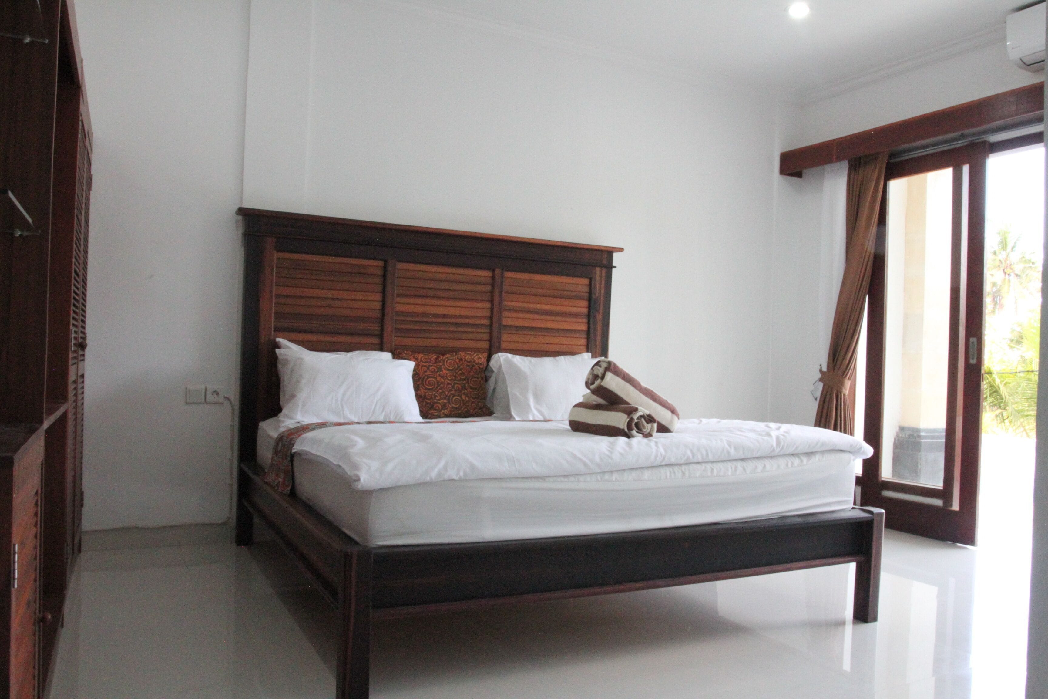 A large bed with a wooden headboard, white bedding, and a pair of rolled towels.