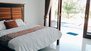 Ein Schlafzimmer mit einem Holz-Kopfteil, einem Bett mit weißer Bettwäsche und einer gemusterten Decke sowie Blick auf einen Pool durch eine Glasdoor.