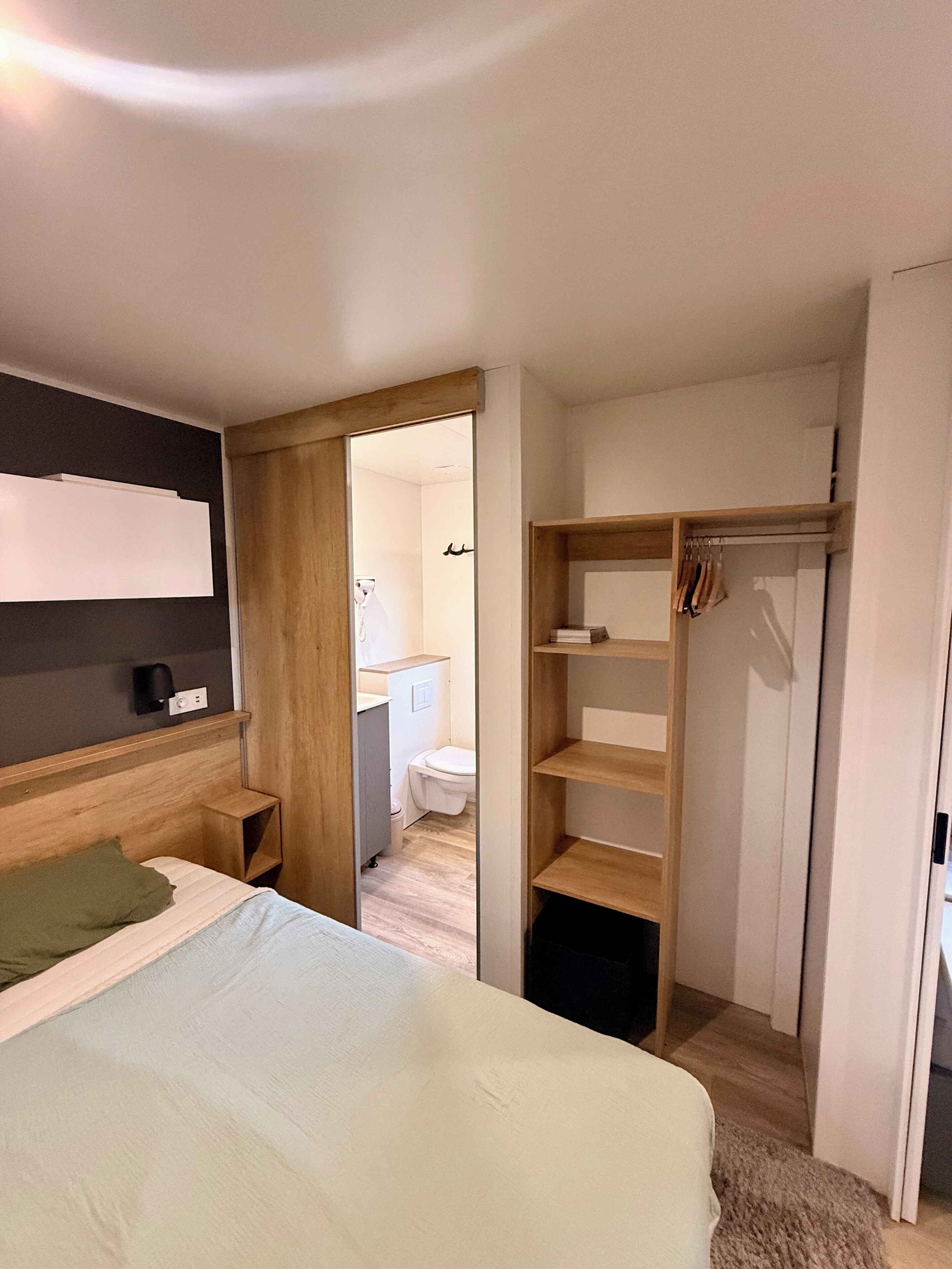A bedroom with a bed, a wooden wardrobe, and a bathroom visible through an open door.
