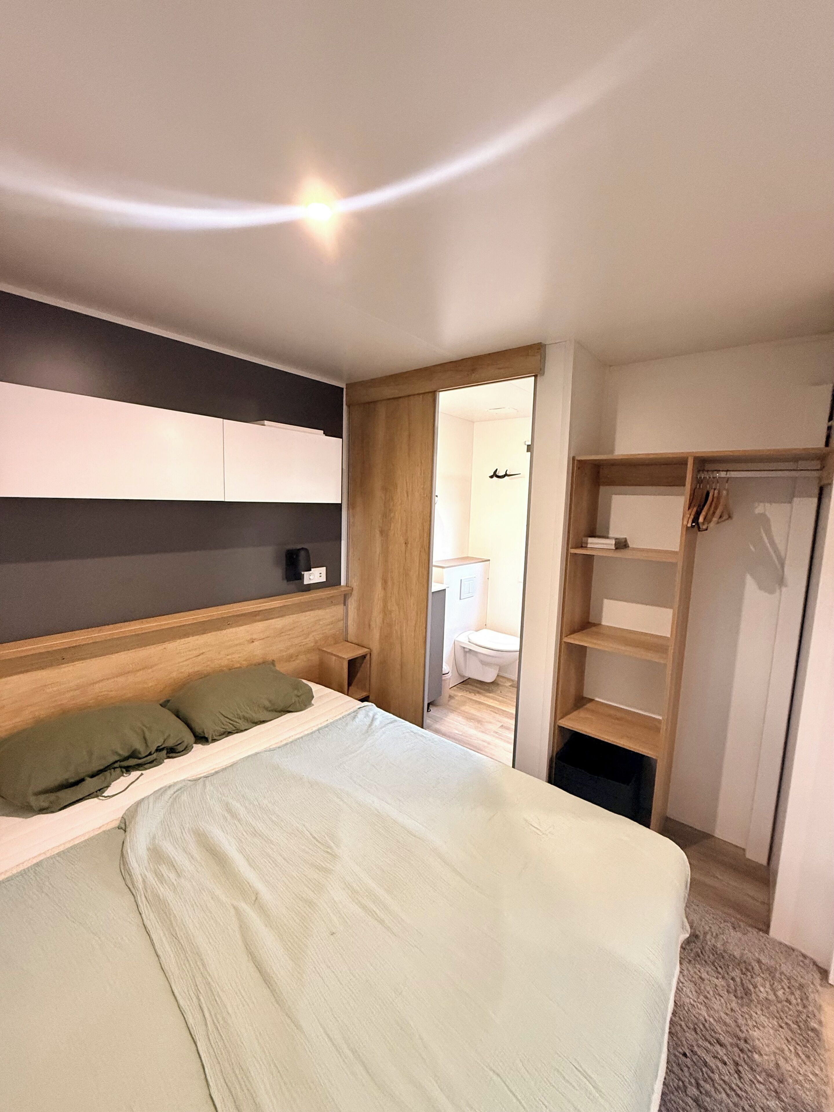 A bedroom with a bed, a wooden wardrobe, and a bathroom visible through an open door.
