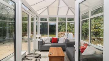 A conservatory with a sofa, cushions, and a wooden table.