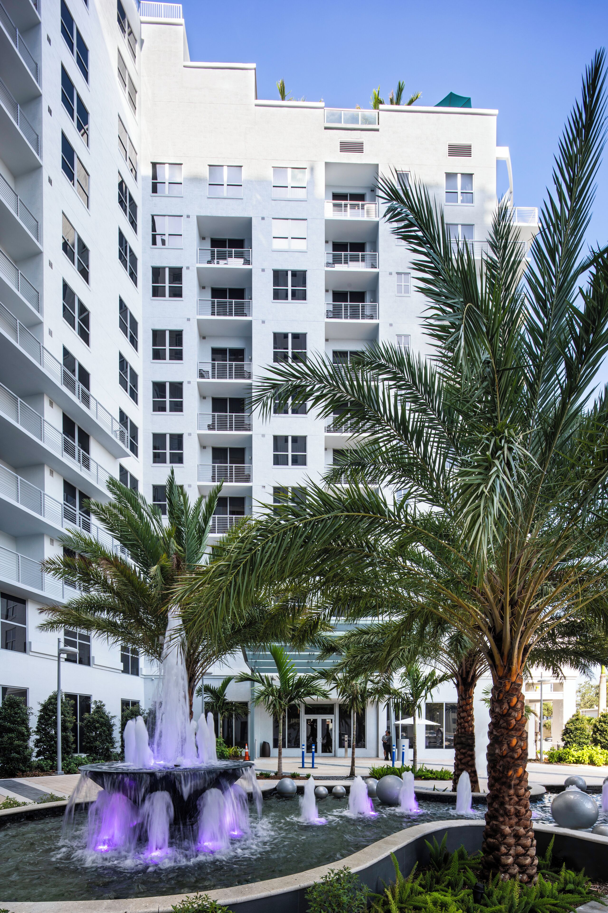 A modern building with multiple balconies and a central water feature with fountains.
