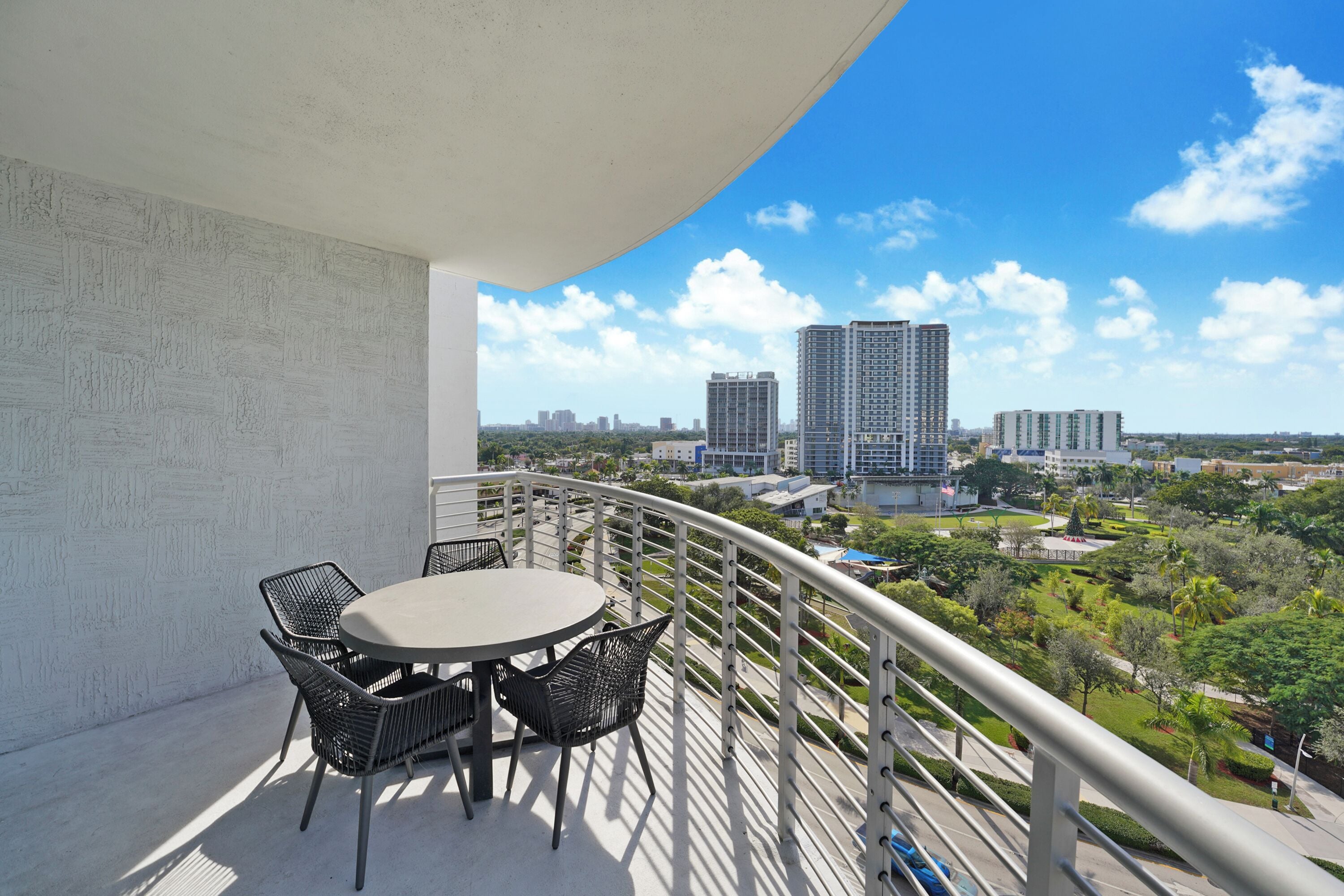 A balcony with a round table and chairs, overlooking a cityscape with high-rise buildings and a park.