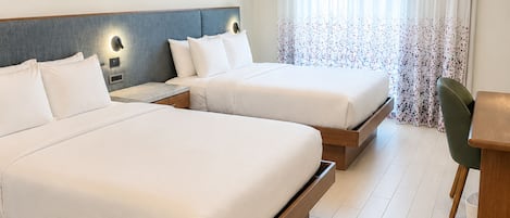 Ein Hotelzimmer mit zwei Betten, einem Schreibtisch und einem Stuhl. Zwei Gemälde hängen an der Wand, und das Zimmer hat ein modernes Design mit einem hellen Boden.