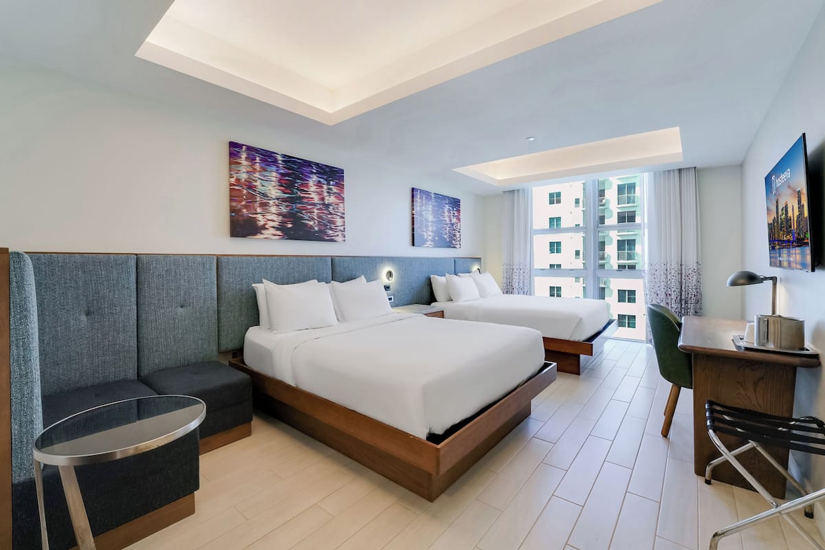 A modern hotel room with two beds, a desk, and a seating area.