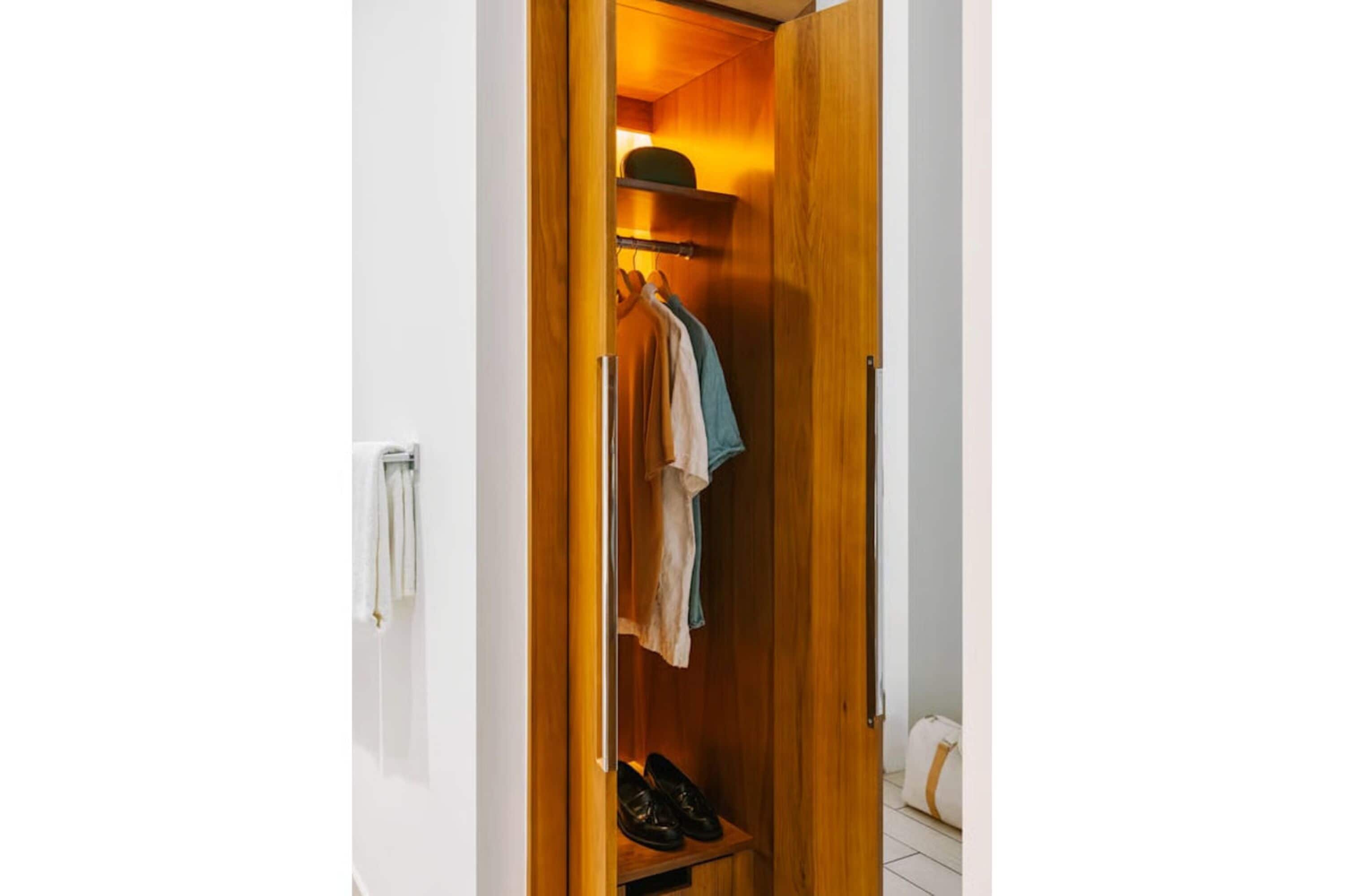A wooden wardrobe with hanging clothes and shoes.