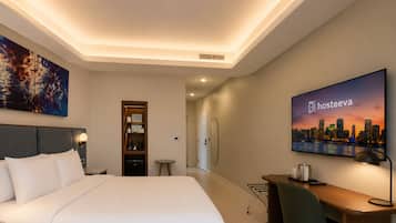 Een hotelkamer met een bed, een bureau, een stoel, een televisie en een boekenplank.