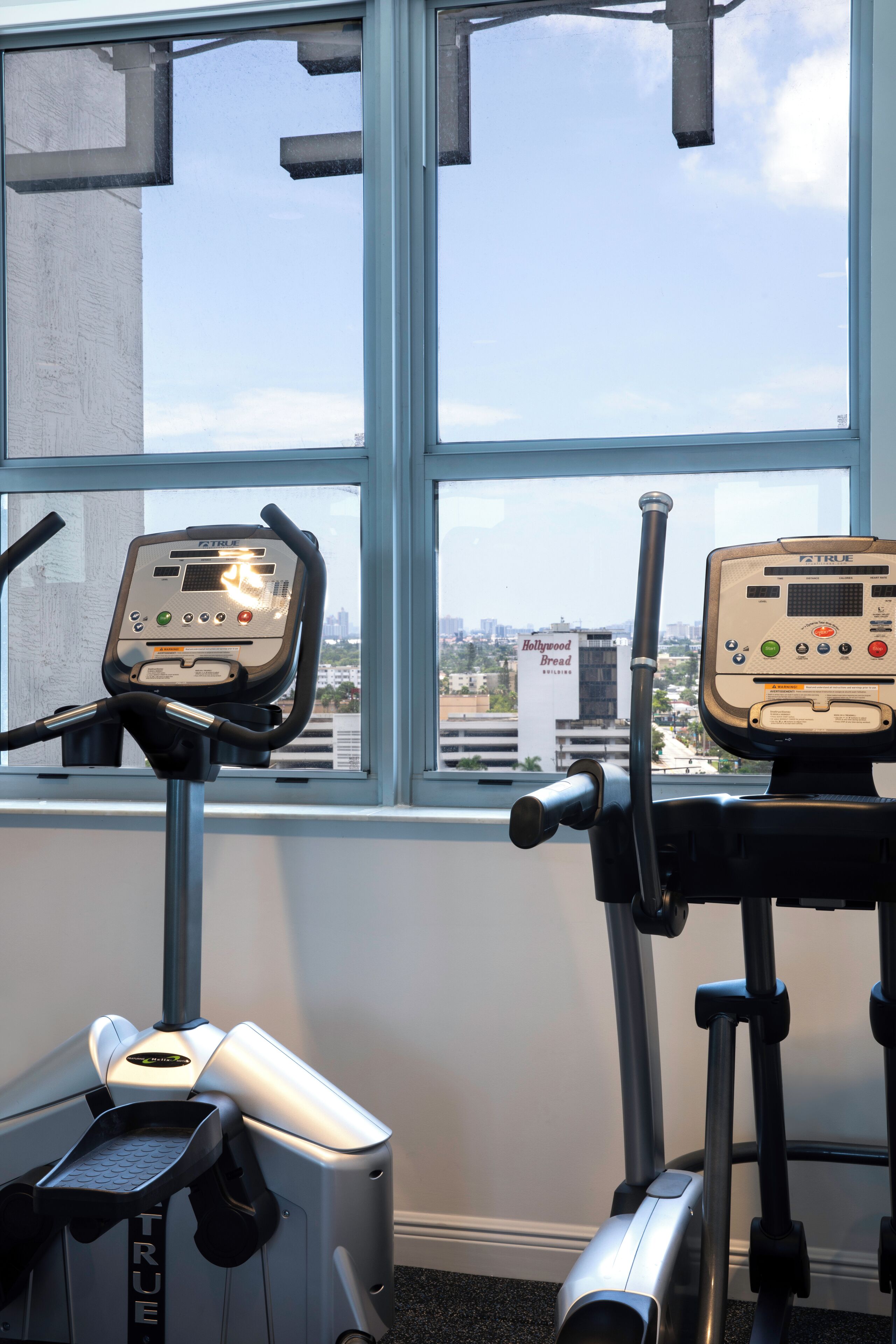 Two exercise machines in a room with a large window.