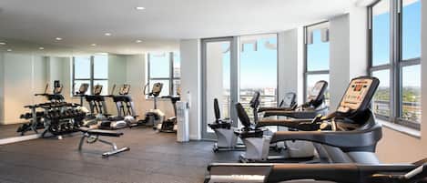 Un gimnasio moderno con diversas máquinas de cardio, equipo de levantamiento de pesas y mancuernas.