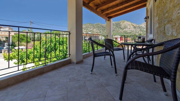 Ein Balkon mit Korbstühlen, einem Tisch und Blick auf Grünflächen und Berge.