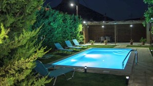 Ein Schwimmbecken mit Liegestühlen, umgeben von Grünpflanzen und einer Holzkonstruktion.