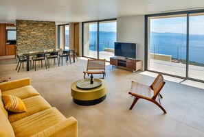 A modern living room with a large TV, a dining area, and a sofa. - Luxurious Architect-designed Property Pool sea View (Cargese)