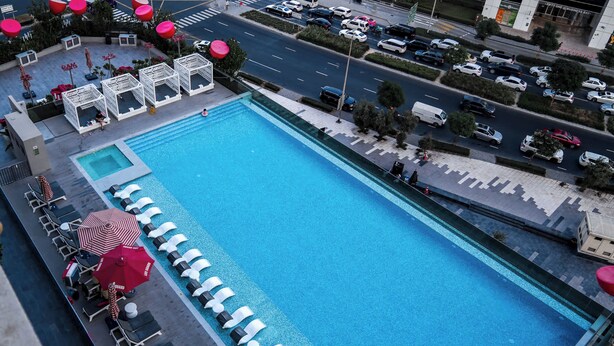 A large outdoor swimming pool with lounge chairs and umbrellas, surrounded by a parking area and a road. - Stayshort - Studio in Business bay Sleeps 2 With City Views (Dubai)