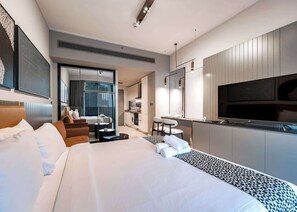A modern hotel room with a large bed, a sitting area with a desk, a kitchenette, and a TV. - Stayshort - Studio in Business bay Sleeps 2 With City Views (Dubai)