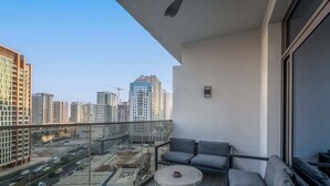 A balcony with a sofa, a small round table, and a view of a cityscape with high-rise buildings and construction. - Stayshort - Studio in Business bay Sleeps 2 With City Views (Dubai)
