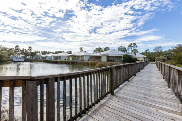 A wooden boardwalk leading to a row of houses by a calm body of water, with a clear sky above. - Villa Rose-Location X3! Close To Wharf, Festivals, Golf, Food, Fun! (Orange Beach)