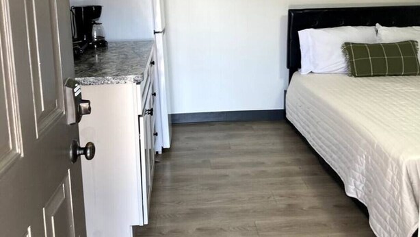 A compact room with a kitchenette, a bed with a green pillow, and a framed picture on the wall. - Boutique Motel in Akron (Akron)