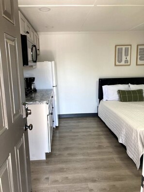 A compact room with a kitchenette, a bed with a green pillow, and a framed picture on the wall. - Boutique Motel in Akron (Akron)