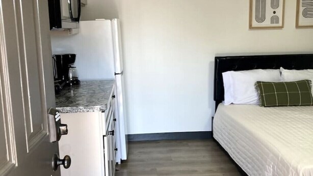 A compact room with a kitchenette, a bed with white bedding and a green pillow, and a wooden floor. - Boutique Motel in Akron (Akron)