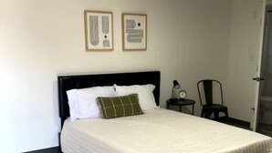 A neatly made bed with a white quilt, a black headboard, and a green pillow. There are two framed abstract artworks on the wall above the bed. - Boutique Motel in Akron (Akron)