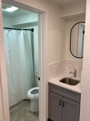 A bathroom with a toilet, a sink, and a shower curtain. - Boutique Motel in Strasburg (Ronks)